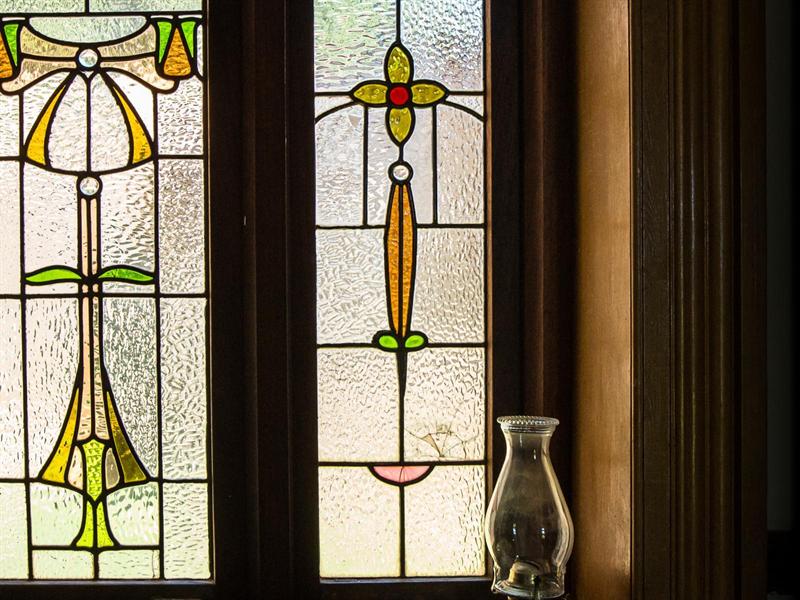 Two original stained glass window panels in amber, green and red, beside a glass lamp chimney